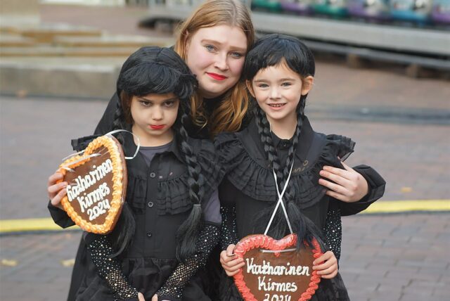 Eine Frau und zwei Kinder mit Lebkuchenherzen „Katharinenkirmes 2024“ stehen auf dem Rathausplatz in Unna.