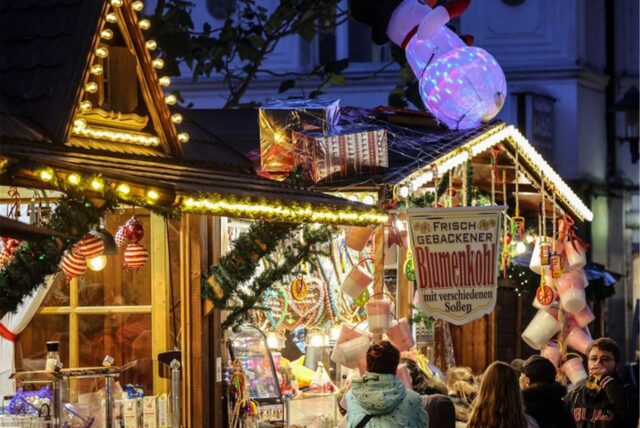 Eine beleuchtete Weihnachtsmarkt-Hütte mit Menschen davor.