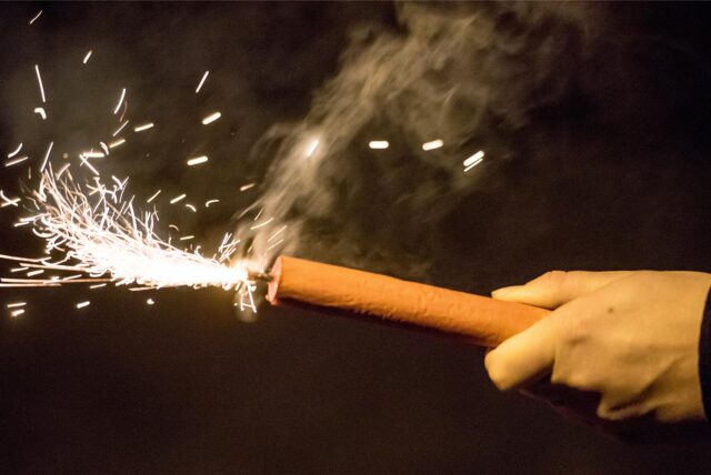 Eine Hand hält einen brennenden Feuerwerkskörper.