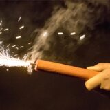 Eine Hand hält einen brennenden Feuerwerkskörper.