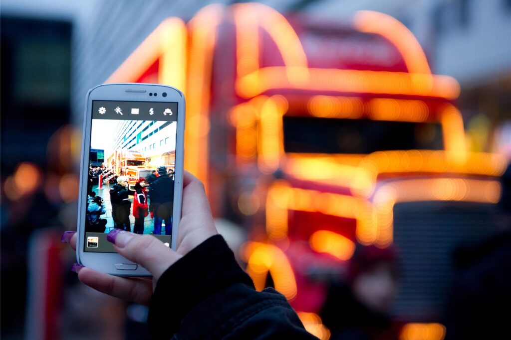 Eine Frau macht ein Foto mit dem Handy vom Coca-Cola Weihnachtstruck. Eine Frau macht ein Foto mit dem Handy vom Coca-Cola Weihnachtstruck.