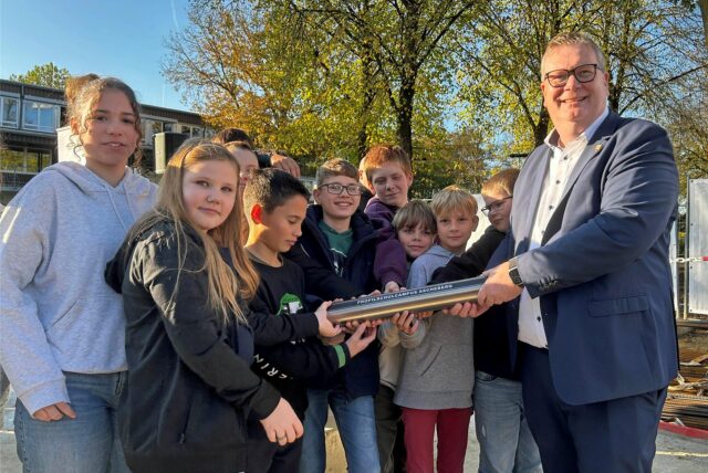 Aschebergs Bürgermeister Thomas Stohldreier und Schüler halten eine Zeitkapsel.