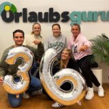 Mitarbeiter von Urlaubsguru halten Ballons, die die Zahl 36 darstellen. Damit weisen sie auf die bald eingeführte 36-Stunden-Woche hin