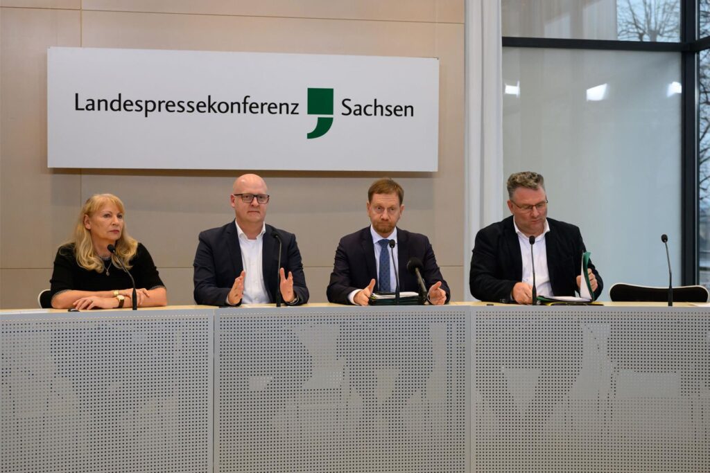 Petra Köpping (SPD, l-r), Sozialministerin von Sachsen, Henning Homann, Co-Vorsitzender der SPD in Sachsen, Michael Kretschmer (CDU), Ministerpräsident von Sachsen, und Christian Hartmann (CDU), Fraktionsvorsitzender im Sächsischen Landtag, sitzen während einer Pressekonferenz im Sächsischen Landtag auf dem Podium.