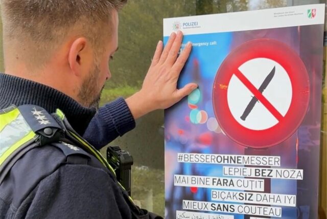 Ein Polizeibeamter hängt in Dortmund ein Plakat der Aktion „Besser ohne Messer“ auf.