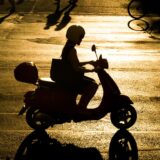 Eine Frau fährt mit einem Roller über eine Straße.