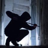 Ein „Einbrecher“ hebelt mit einem Brecheisen eine Tür im Keller eines Wohnhauses auf (gestellte Szene)