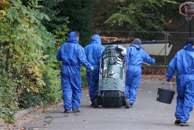 Arbeiter in Overalls ziehen ein Reinigungsgerät zu einem Grundstück.