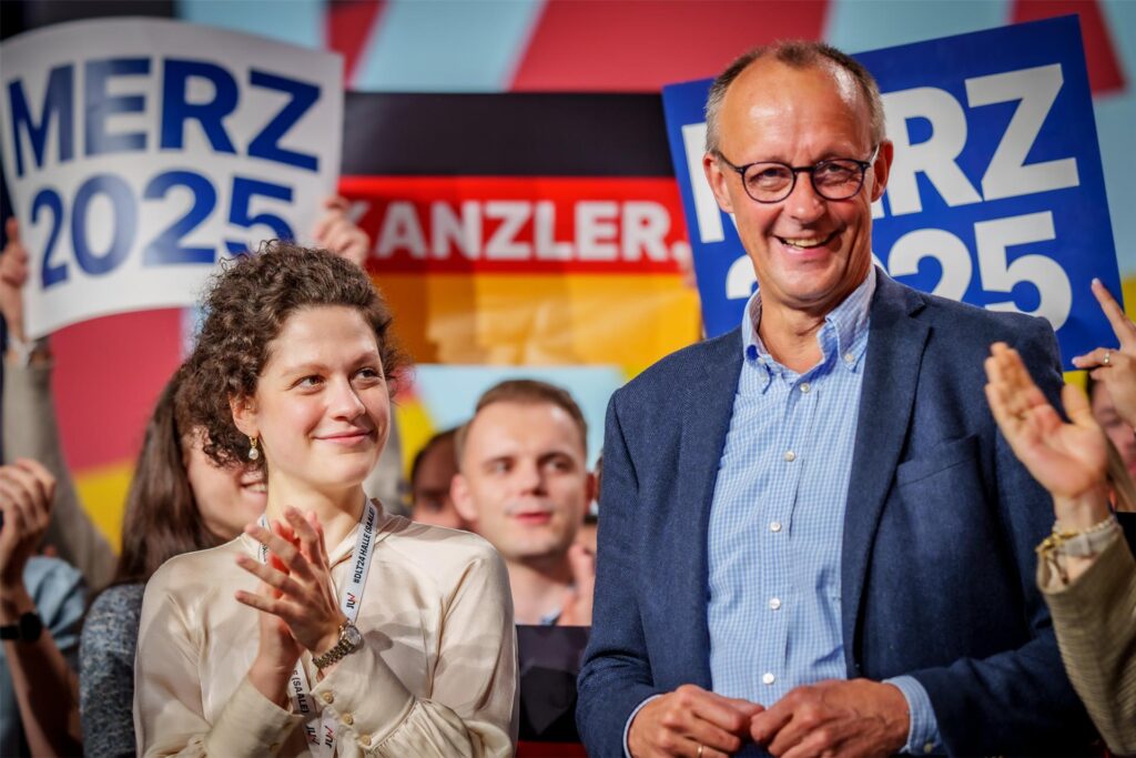 Sarah Beckhoff steht beim Deutschlandtag der Jungen Union neben CDU-Kanzlerkandidat Friedrich Merz, klatscht und lächelt ihm zu. Friedrich Merz lacht vergnügt in die Menge.