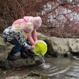 Linn und Matilda halten einen Eimer in die Ruhr, aus dem Fische freigelassen werden.