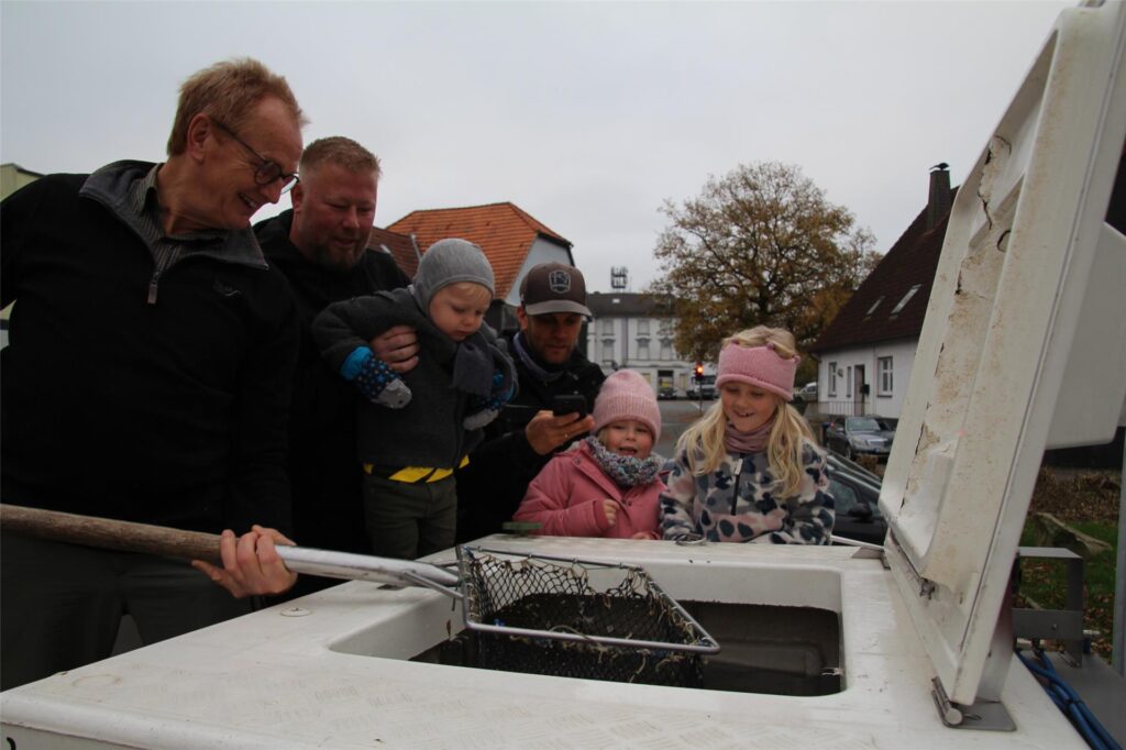 Eine Gruppe Menschen steht um das Bassin des Lastwagens herum und schaut auf die Fischer im Kescher. Eine Gruppe Menschen steht um das Bassin des Lastwagens herum und schaut auf die Fischer im Kescher.