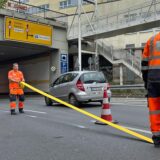 Zwei Männer mit Signalkleidung kleben eine gelbe Linie auf die Straße vor dem Ringtunnel in Unna. Neben ihnen fährt ein Auto vorbei.