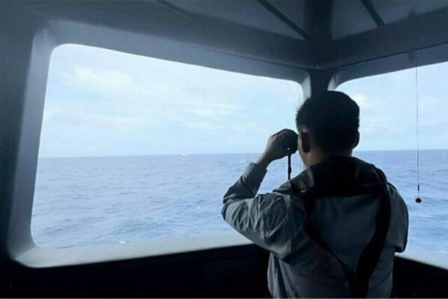 Ein Mitarbeiter der Seesicherheitsbehörde bewacht mit einem Fernglas die Bewegungen eines Schiffes der chinesischen Küstenwache im Meer.