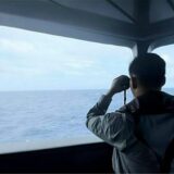 Ein Mitarbeiter der Seesicherheitsbehörde bewacht mit einem Fernglas die Bewegungen eines Schiffes der chinesischen Küstenwache im Meer.