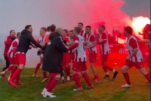 Die Spieler des TuS Hemmerde tanzen zum Derbysieg. Im Hintergrund zünden die mitgereisten Fans Pyro.
