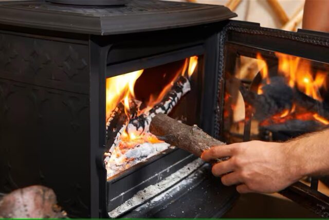 Eine Hand wirft Holz in den brennenden Kamin.