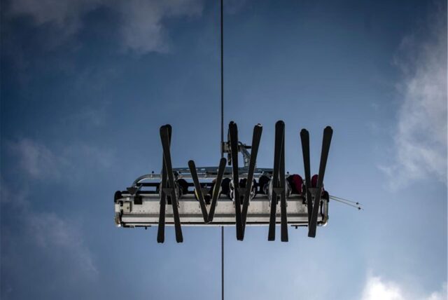 Skier in einem Lift zeichnen sich vor dem blauen Himmel ab.