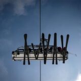 Skier in einem Lift zeichnen sich vor dem blauen Himmel ab.