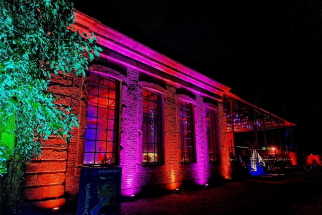 Hertens Orangerie im Schlosspark bei Nacht, hier in den Lichtfarben Rot und Lila illuminiert.