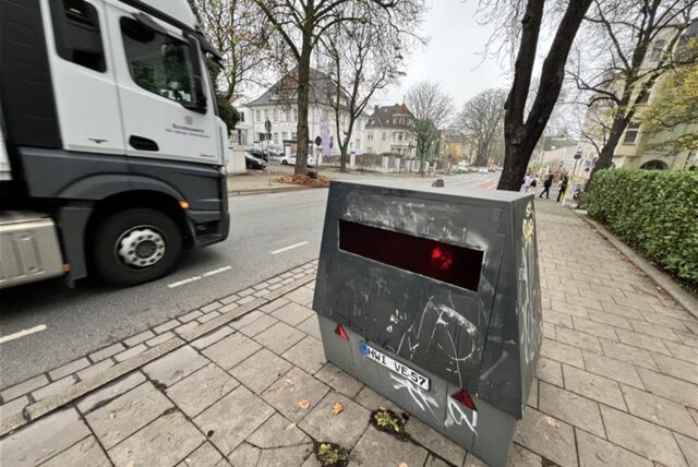 Ein beschmierter Enforcement Trailer des Kreises steht auf dem Bürgersteig der Friedrich-Ebert-Straße in Unna. Links im Bild ist ein Lkw auf der Straße zu sehen.
