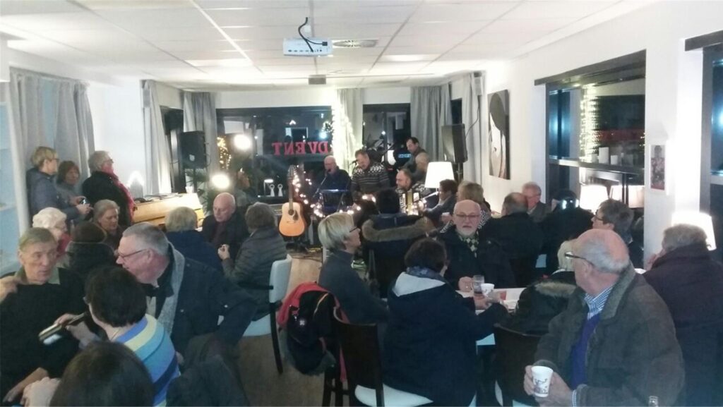 Ein Adventsfenster hat sich im Dorfcafé in Ardey geöffnet. Männer und Frauen sitzen gemütlich bei einem Heißgetränk zusammen. Im Hintergrund spielt eine Band Musik. (Archivbild).