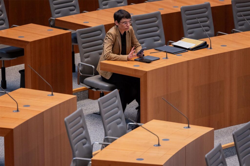 Josefine Paul sitzt im Plenum des Landtags an einem Tisch und schaut in ihr Handy.