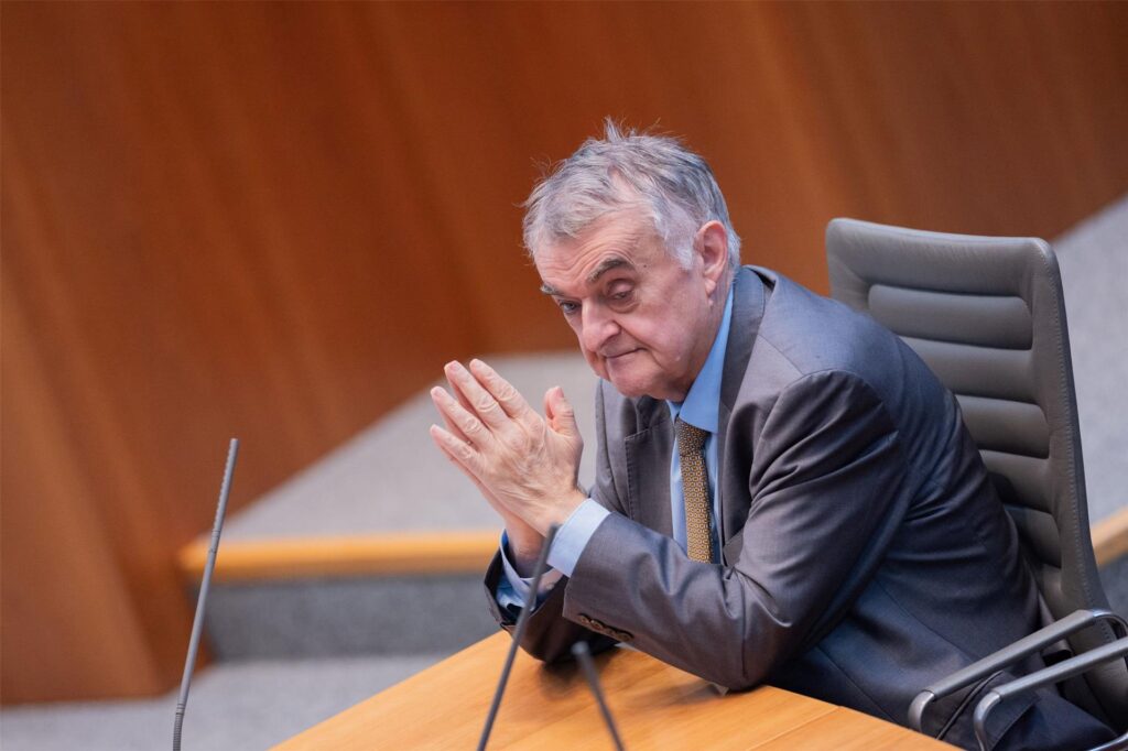 Herbert Reul sitzt in einem Anzug an einem Tisch und hat die Handflächen aneinander gelegt.