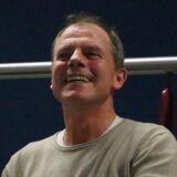 Holger Schöße (r.) freut sich und schlägt auf eine Klatschpappe. Neben ihm grinst jemand.