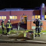 Feuerwehrleute stehen vor der Sporthalle am Kleiweg in Bergkamen-Weddinghofen. Schläuche sind ausgerollt und für einen Wassereinsatz vorbereitet.
