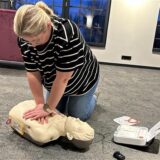 Frau zeigt Herzdruck-Massage an einer Puppe