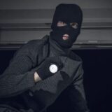 Ein maskierter Einbrecher mit einer Taschenlampe in der Hand steigt durch ein Fenster. (gestellte Szene)