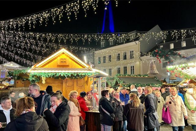 Der Weihnachtsmarkt 2024 in Unna. Viele Menschen haben sich auf dem Alten Markt versammelt und genießen die Weihnachtszeit. Im Hintergrund ist der blau beleuchtete Kirchturm zu sehen.