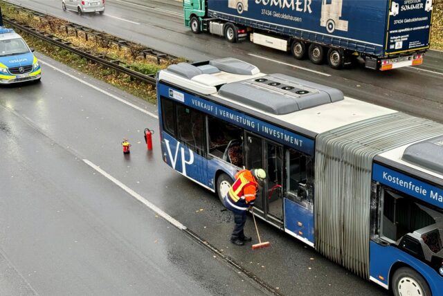 Einsatzkräfte der Polizei und Feuerwehr stehen neben einem beschädigten Gelenkbus.