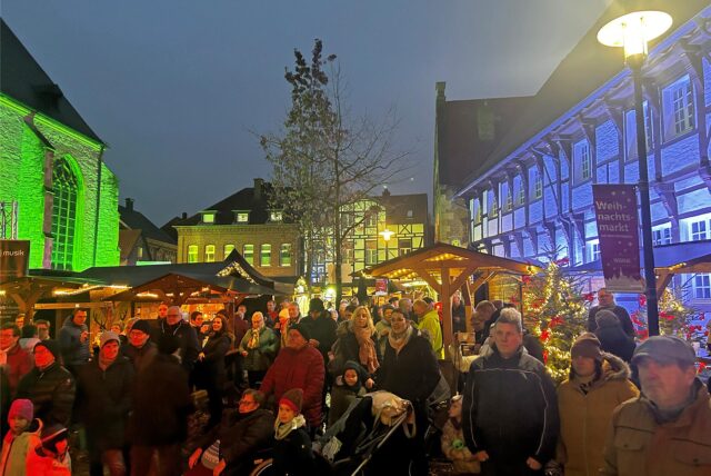 Besucher gehen abends über den erleuchteten Weihnachtsmarkt 2023 auf dem Kirchhof in Werne
