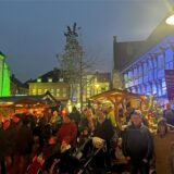 Besucher gehen abends über den erleuchteten Weihnachtsmarkt 2023 auf dem Kirchhof in Werne
