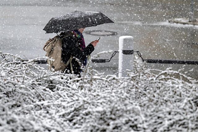 Eine Person geht mit einem Regenschirm während es schneit.