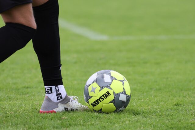 Ein Derbystar-Fußball liegt auf dem Rasen. Ein Fußballer spielt ihn mit dem Fuß.