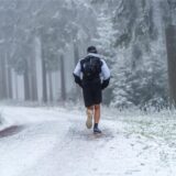 Ein Trailrunner läuft in kurzer Hose auf einem schneebedeckten Waldweg Richtung Feldberggipfel. 