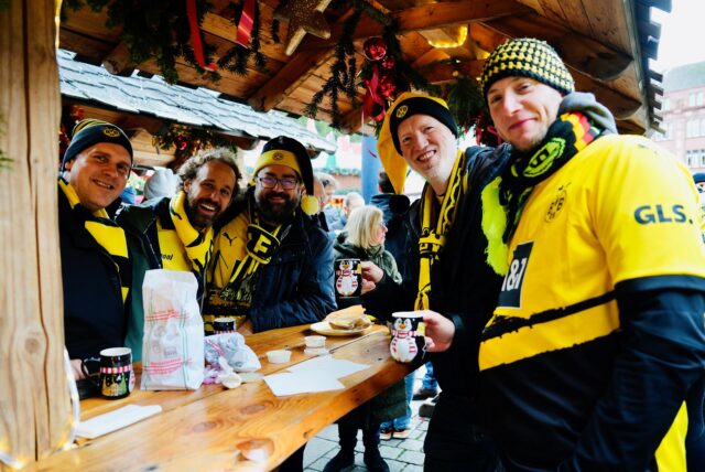 BVB-Fans stehen an einem Glühweinstand auf dem Dortmunder Weihnachtsmarkt.