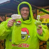 Christoph Scheiding steht in einem neongrünen Hoodie mit der Aufschrift „Ich hasse Menschen“ vor seinem Stand auf dem Dortmunder Weihnachtsmarkt.