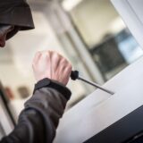 Ein Einbrecher versucht mit einem Schraubenzieher ein Fenster zu öffnen (gestellte Szene)