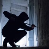 Ein „Einbrecher“ hebelt mit einem Brecheisen eine Tür im Keller eines Wohnhauses auf (gestellte Szene).