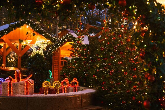 Geschmückte Weihnachtsbäume und beleuchtete Buden und Geschenke bei Schnee auf einem Weihnachtsmarkt.