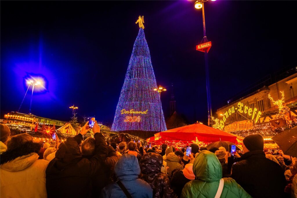 Besucher des Dortmunder Weihnachtsmarktes 2024 schauen auf den beleuchten Weihnachtsbaum. Besucher des Dortmunder Weihnachtsmarktes 2024 schauen auf den beleuchten Weihnachtsbaum.