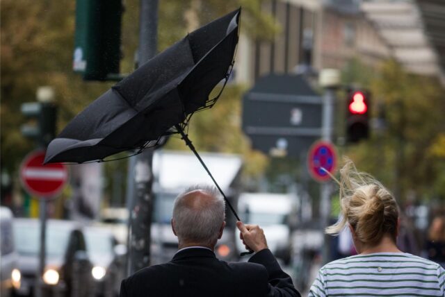 Der Schirm eines Passanten klappt in der Innnenstadt bei Sturm und Regen um.