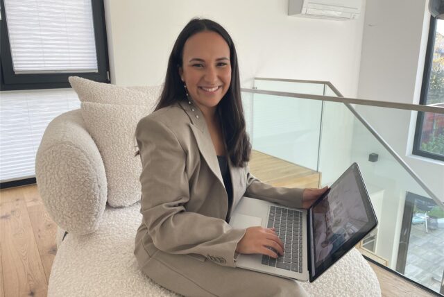 Die Dortmunder Immobilienmaklerin Asma Boufeljat sitzt auf einem Sofa und ht einen Laptop auf dem Schoß.