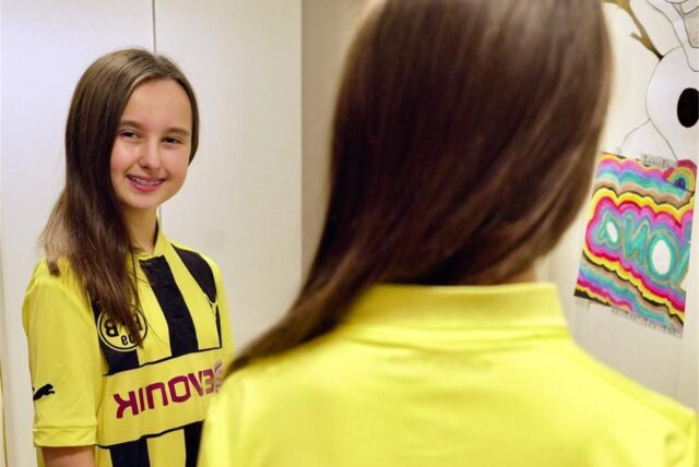 Kiara Santana aus Lütgendortmund steht im BVB-Trikot vor dem Spiegel.