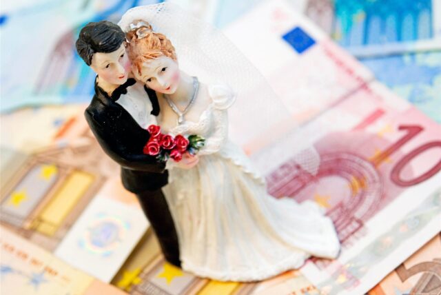 Eine kleine Figur eines Hochzeitspaares steht auf mehreren ausgebreiteten Euro-Scheinen