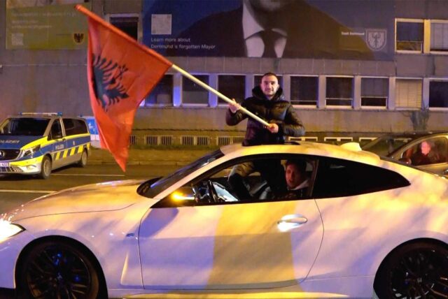 Zwei Männer fahren zum albanischen Nationalfeiertag mit ihrem Auto auf dem Wall in Dortmund und schwenken eine Albanien-Fahne.