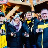 Vier BVB-Fans stehen vor einer Glühweinhütte auf dem Dortmunder Weihnachtsmarkt und trinken aus einer Pinguin-Tasse.